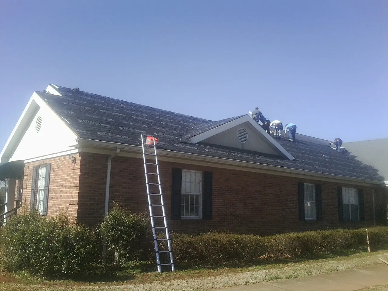 Crew tearing shingles off a brick ranch roof with a ladder set — Metal Roof Repair work by our crew in Kingsley