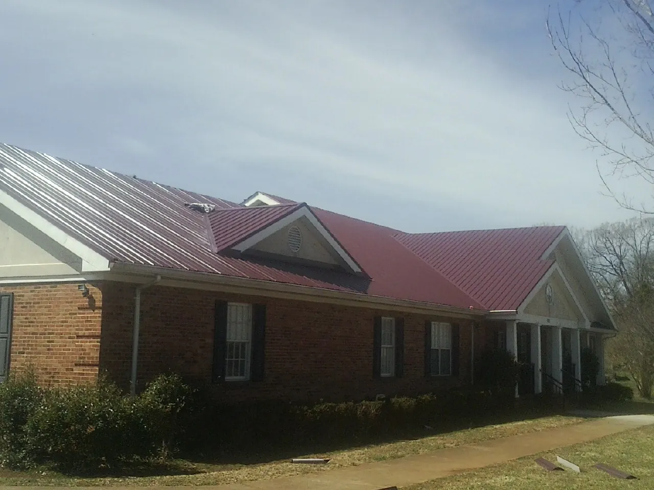 Red metal roof with gabled entries on a long brick building, from a Hail Damage Roof Repair job in Kingsley