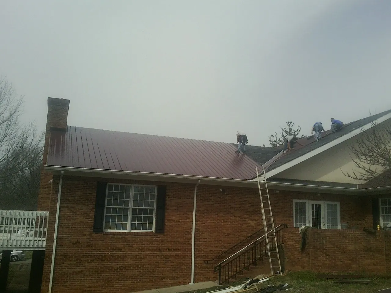 Crew setting red metal roofing panels on a brick home in Kingsley