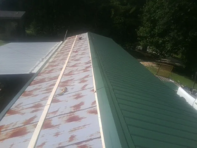 Old rusted panels beside newly installed green metal roofing — Wind Damage Roof Repair by Roofing Brothers in Kingsley