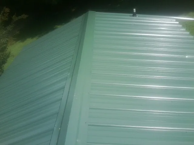 New green metal panels meeting at the ridge of a roof — Flat Roof Repair work by our crew in Kingsley