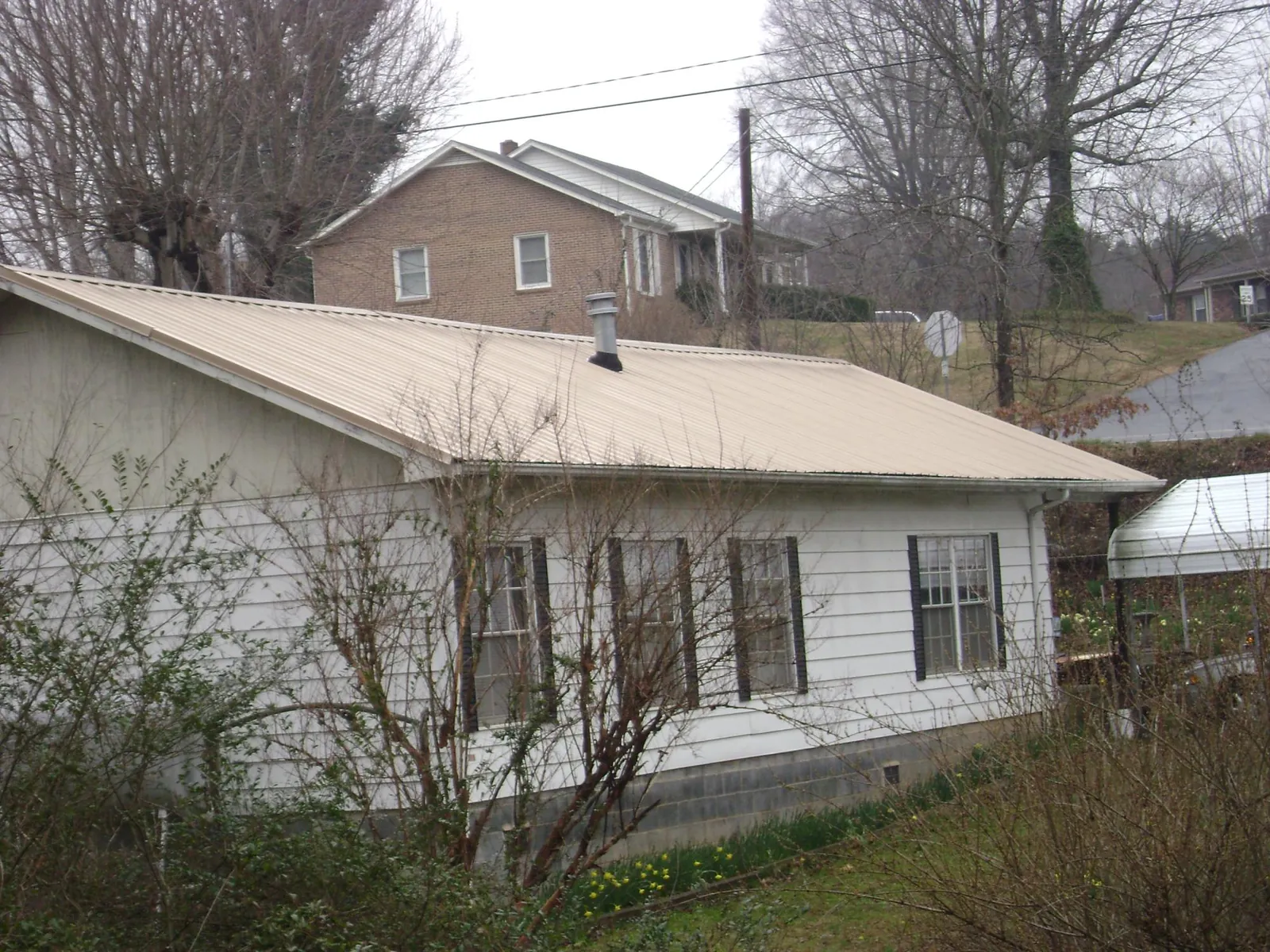 Tan metal roof on a white sided house set into a hillside — Commercial Roofing by Roofing Brothers in Kingsley