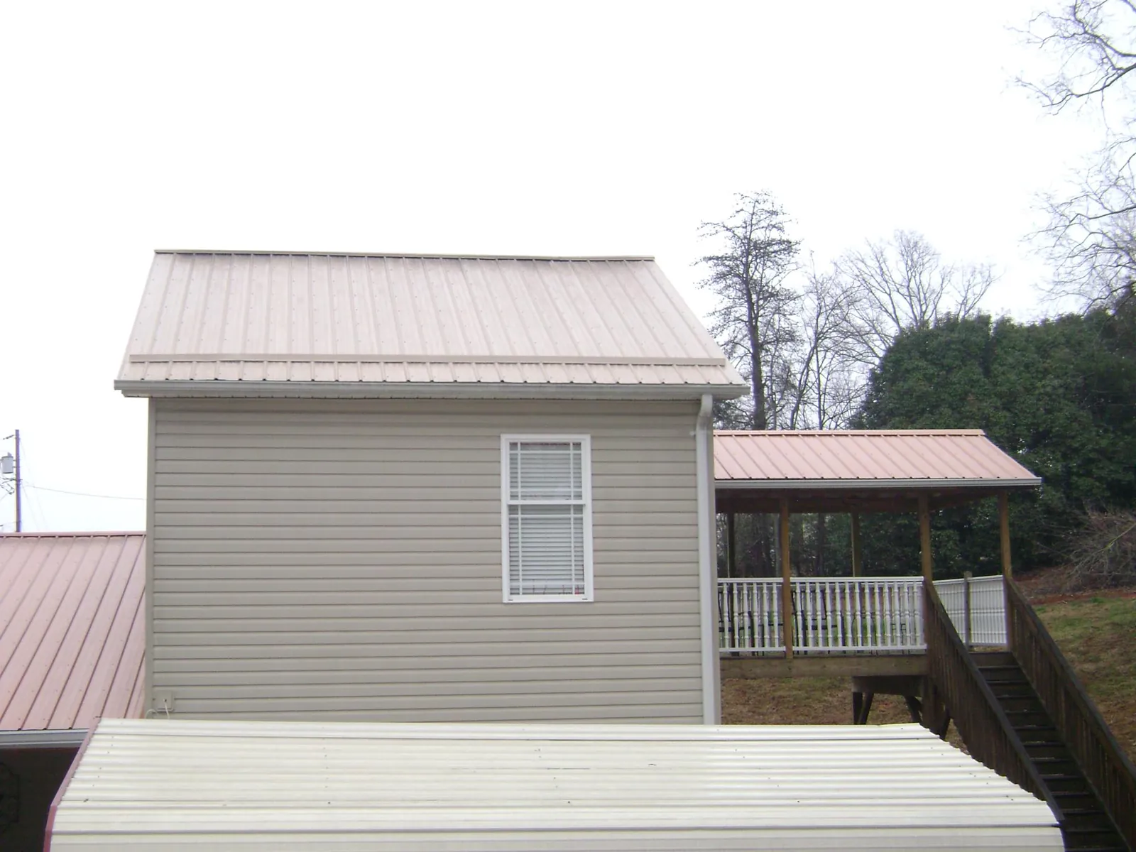 Tan metal roofs on a two story addition and attached porch, from a Roof Replacement job in Kingsley